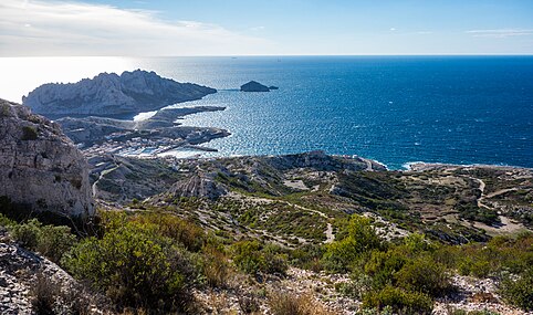 Vue depuis le massif de Marseilleveyre, sur la gauche et successivement de l’avant-plan à l’arrière-plan : rocher Saint Michel, port des Goudes sa digue et son éperon, pointe du cap Croisette, île Maïre, île Tiboulen.