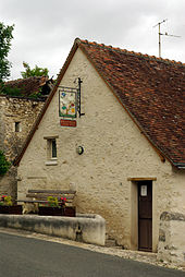 Photographie du pignon d'un bâtiment et de sa porte d'entrée surmontée d'une enseigne en ferronnerie.