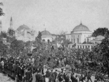 photographie noir et blanc : une foule dans la rue devant des bâtiments à dôme et minarets