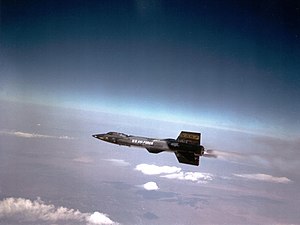 Black rocket aircraft with stubby wings and short vertical stabilizers above and below tail unit