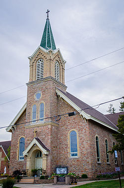 A small fieldstone church with a front-centered steeple constructed of bricks at the upper level