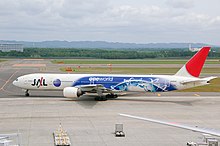 A Boeing 777-300 aircraft with special Oneworld livery taxiing from the tarmac on to the taxiway, with a mountain view on the background