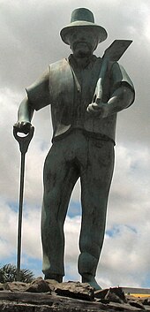 Stone statue of a middle aged-man with a beard, a shovel, and some other similar instrument